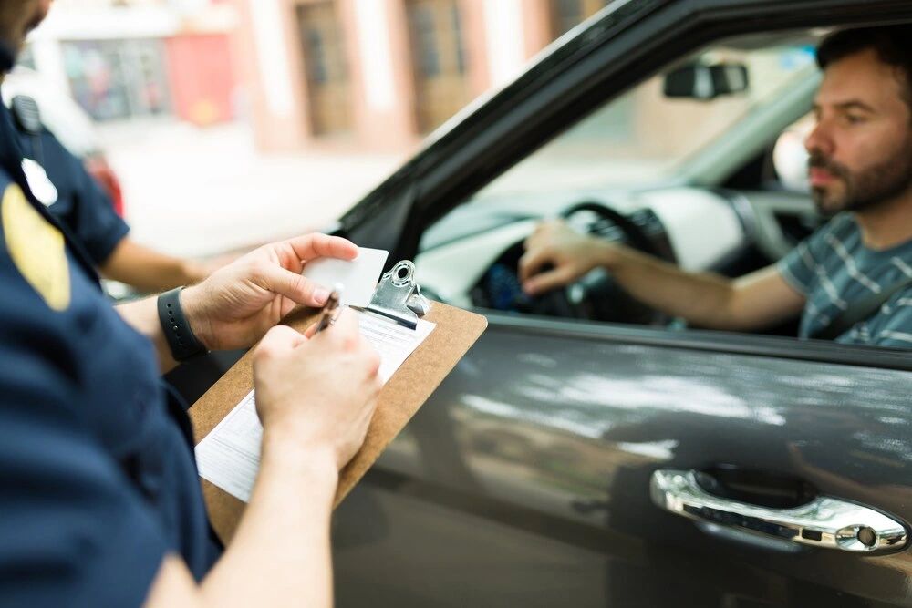 Close up of a police cop writing a traffic ticket or fine to a male driver in his car