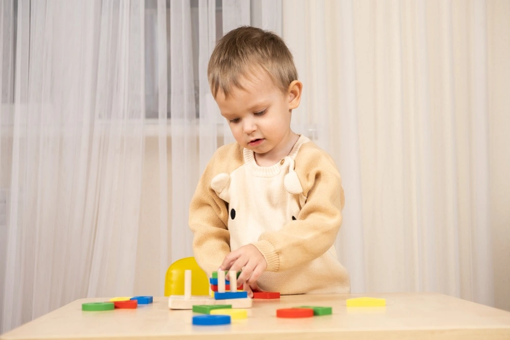 Little cute boy playing with toys while sitting at table