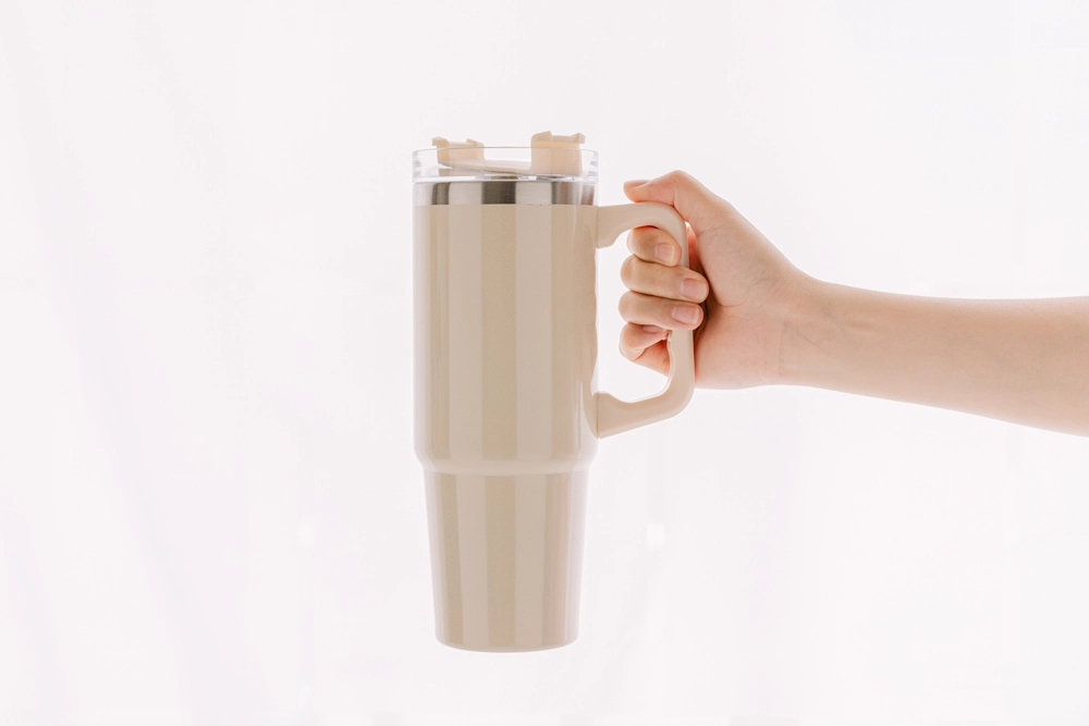 Minimalist Beige Travel Mug with Handle Held by a Hand on White Background